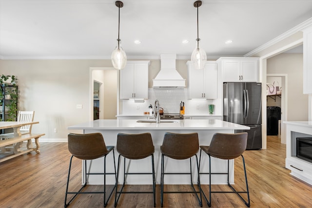 kitchen featuring stainless steel refrigerator, sink, light hardwood / wood-style flooring, decorative light fixtures, and custom exhaust hood