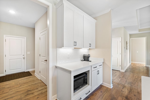 kitchen with hardwood / wood-style flooring, ornamental molding, tasteful backsplash, white cabinetry, and black microwave