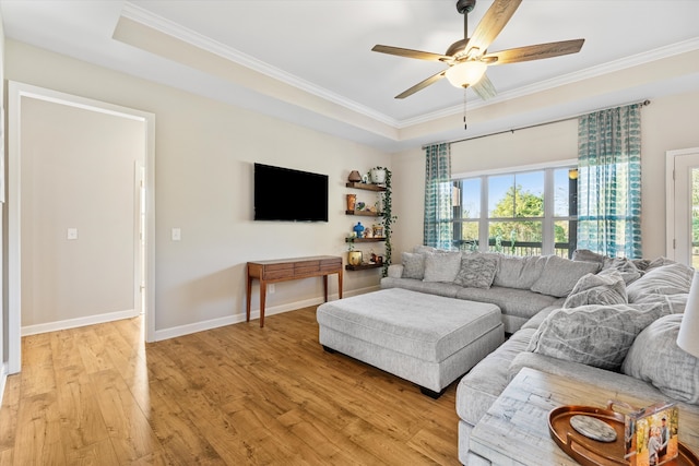 living room featuring ceiling fan, ornamental molding, a tray ceiling, and light hardwood / wood-style flooring