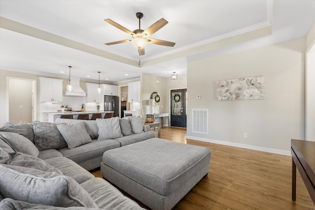 living room with a raised ceiling, crown molding, ceiling fan, and light wood-type flooring