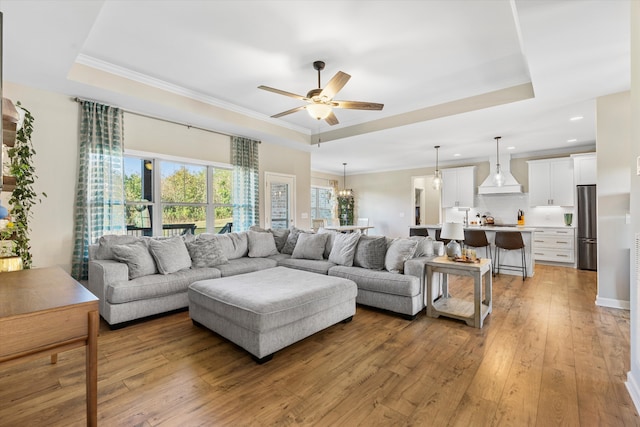 living room featuring ceiling fan, a raised ceiling, light wood-type flooring, and crown molding