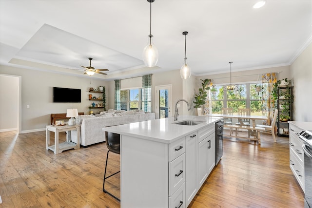 kitchen with light wood-type flooring, a kitchen island with sink, sink, decorative light fixtures, and white cabinets