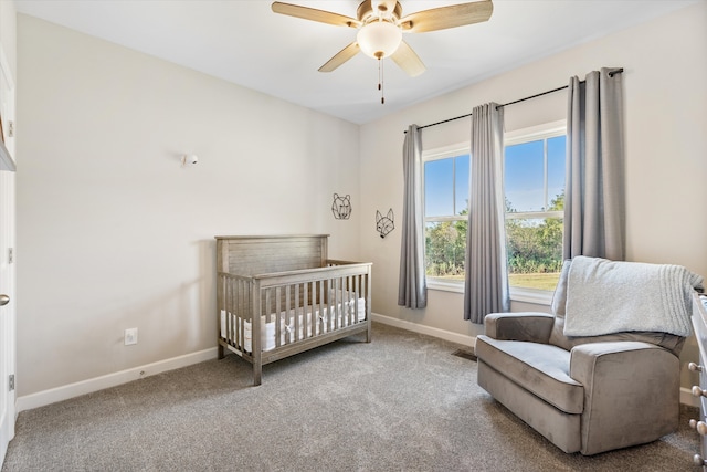 carpeted bedroom featuring multiple windows, ceiling fan, and a crib