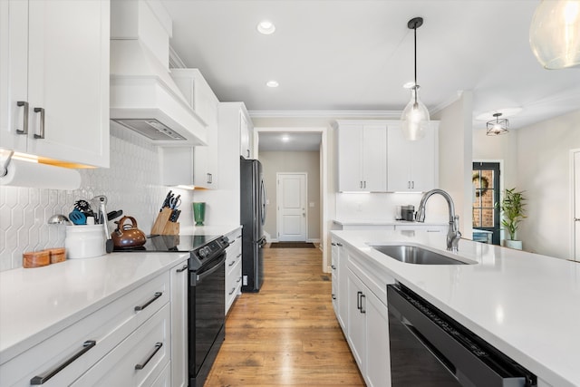 kitchen with white cabinets, black appliances, sink, hanging light fixtures, and custom range hood