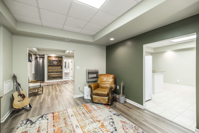 living area with a paneled ceiling, light hardwood / wood-style floors, and heating unit