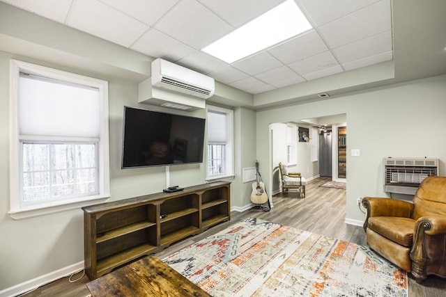 living room featuring wood-type flooring, heating unit, a wall unit AC, and a healthy amount of sunlight