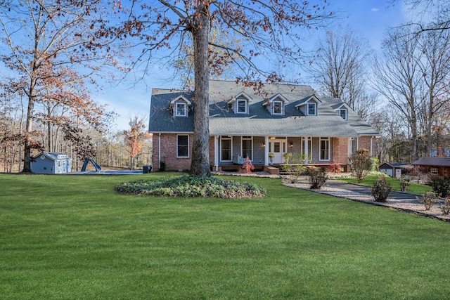 new england style home with a front lawn, covered porch, and a storage shed