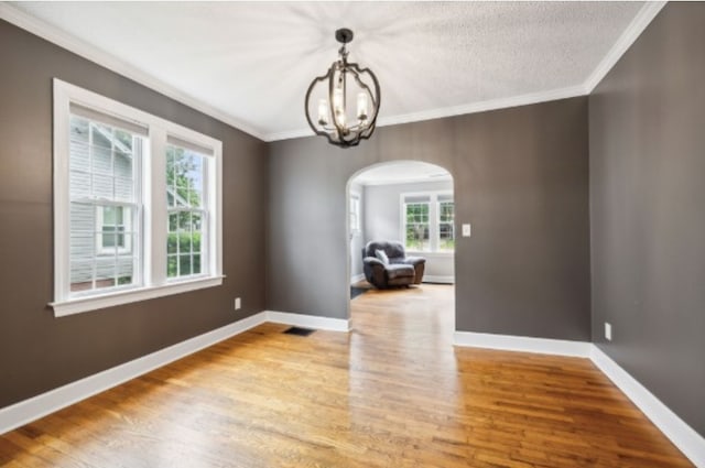 unfurnished dining area featuring crown molding, an inviting chandelier, a textured ceiling, and light wood-type flooring