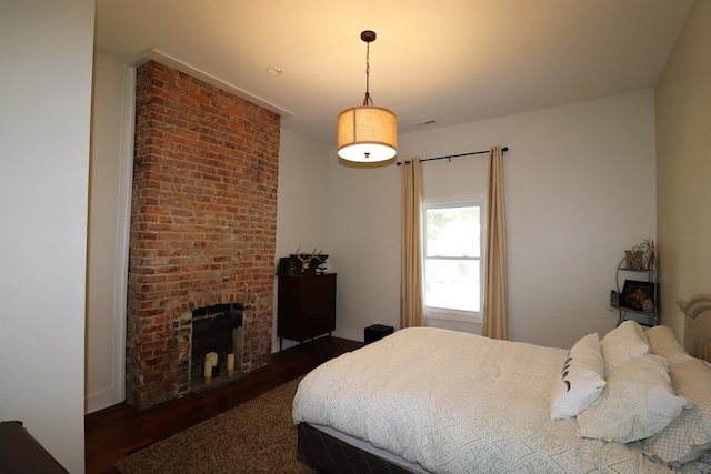 bedroom with dark hardwood / wood-style flooring and a brick fireplace