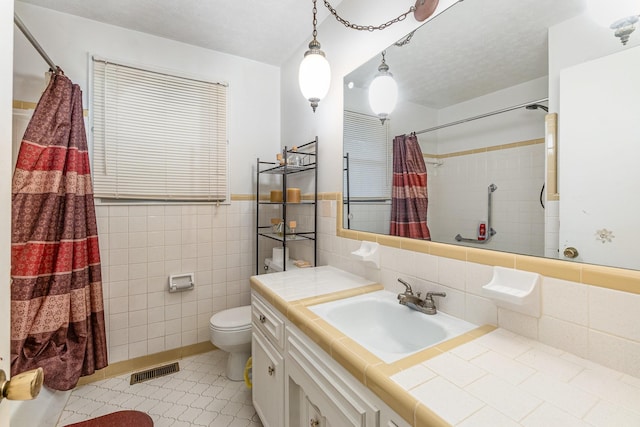 bathroom with tile patterned floors, a textured ceiling, vanity, tile walls, and toilet