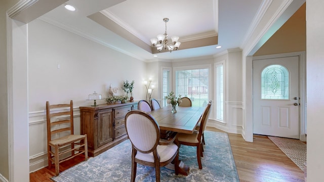 dining space featuring a raised ceiling, crown molding, a chandelier, and light wood-type flooring