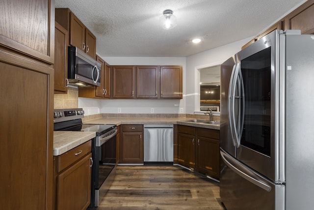 kitchen with appliances with stainless steel finishes, dark hardwood / wood-style flooring, tasteful backsplash, a textured ceiling, and sink