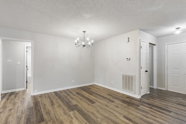 spare room featuring a textured ceiling, dark wood-type flooring, and a chandelier