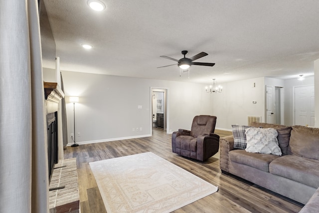 living room with a textured ceiling, ceiling fan with notable chandelier, wood-type flooring, and a fireplace