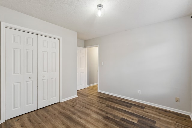 unfurnished bedroom with a textured ceiling, dark wood-type flooring, and a closet