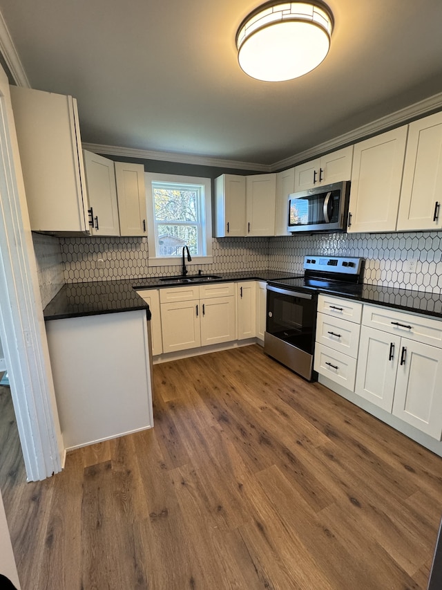 kitchen with stainless steel appliances, dark countertops, white cabinetry, and a sink