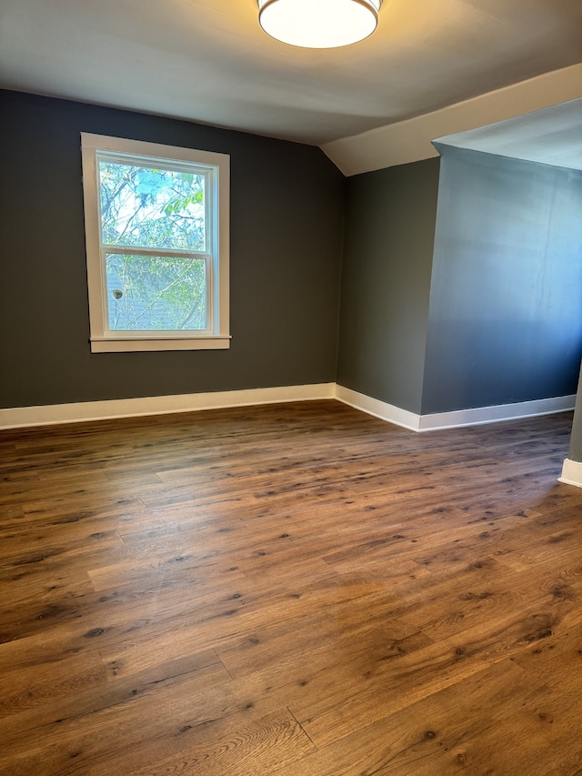 spare room featuring dark wood-style floors, baseboards, and vaulted ceiling