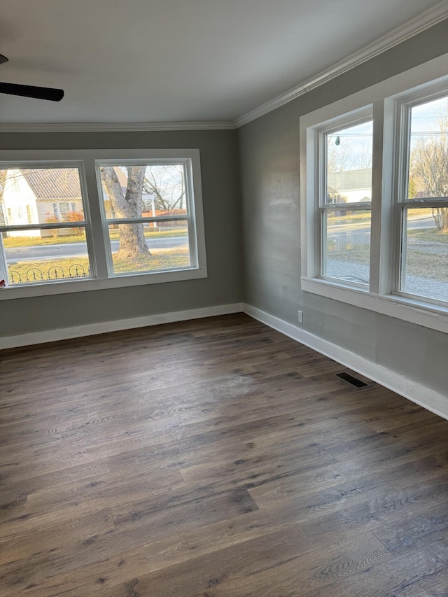 empty room featuring baseboards, visible vents, dark wood-type flooring, and crown molding