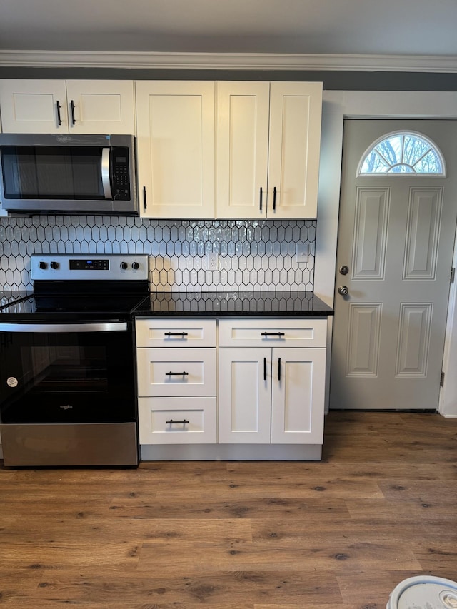 kitchen featuring stainless steel appliances, wood finished floors, white cabinets, decorative backsplash, and dark countertops