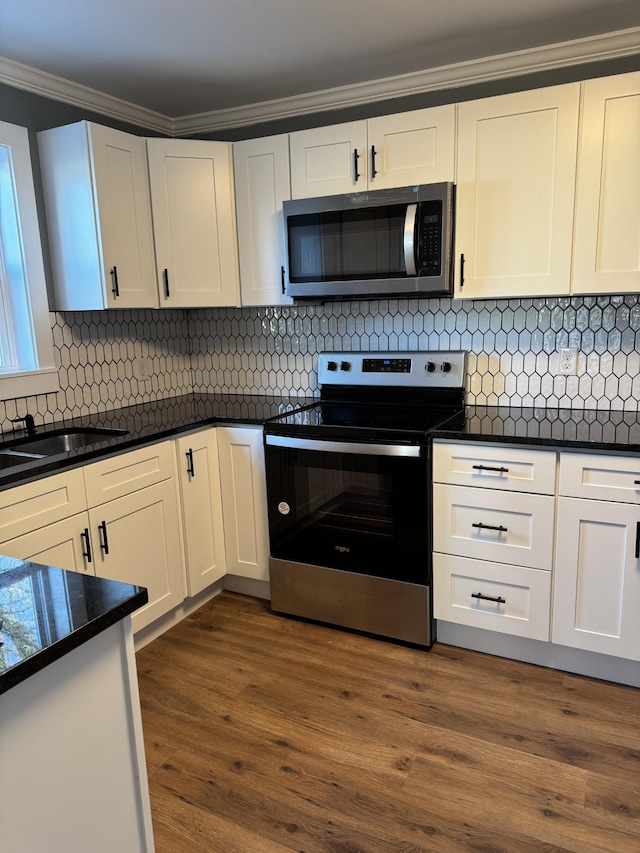 kitchen with appliances with stainless steel finishes, dark countertops, white cabinetry, and dark wood-type flooring