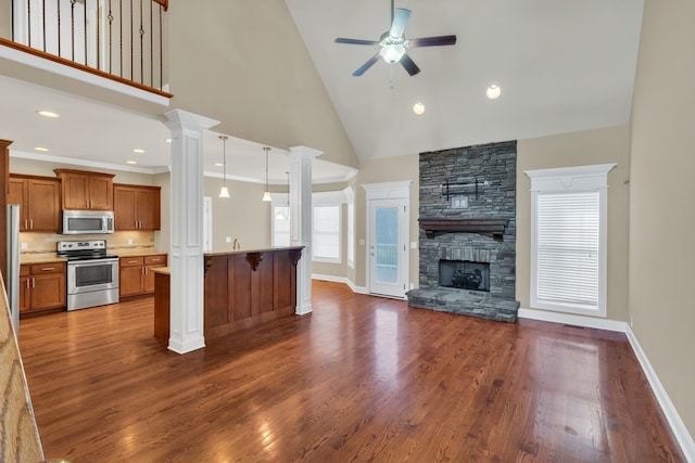 kitchen featuring a breakfast bar, stainless steel appliances, high vaulted ceiling, a stone fireplace, and hanging light fixtures