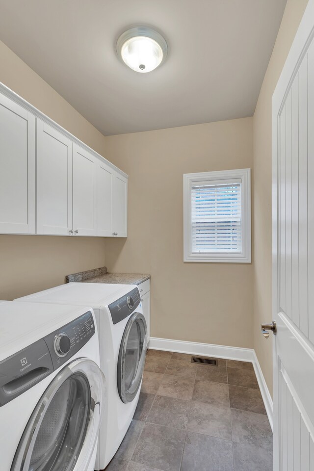 clothes washing area with tile patterned floors, washer and dryer, and cabinets