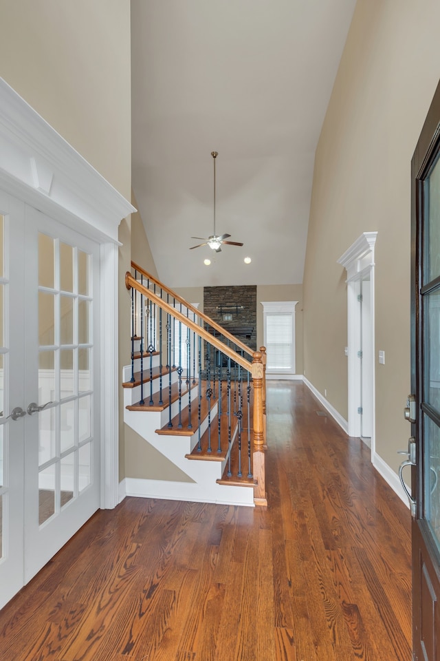 stairs featuring a fireplace, ceiling fan, hardwood / wood-style floors, and high vaulted ceiling