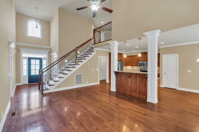 unfurnished living room featuring a high ceiling, dark hardwood / wood-style floors, ornate columns, and ornamental molding