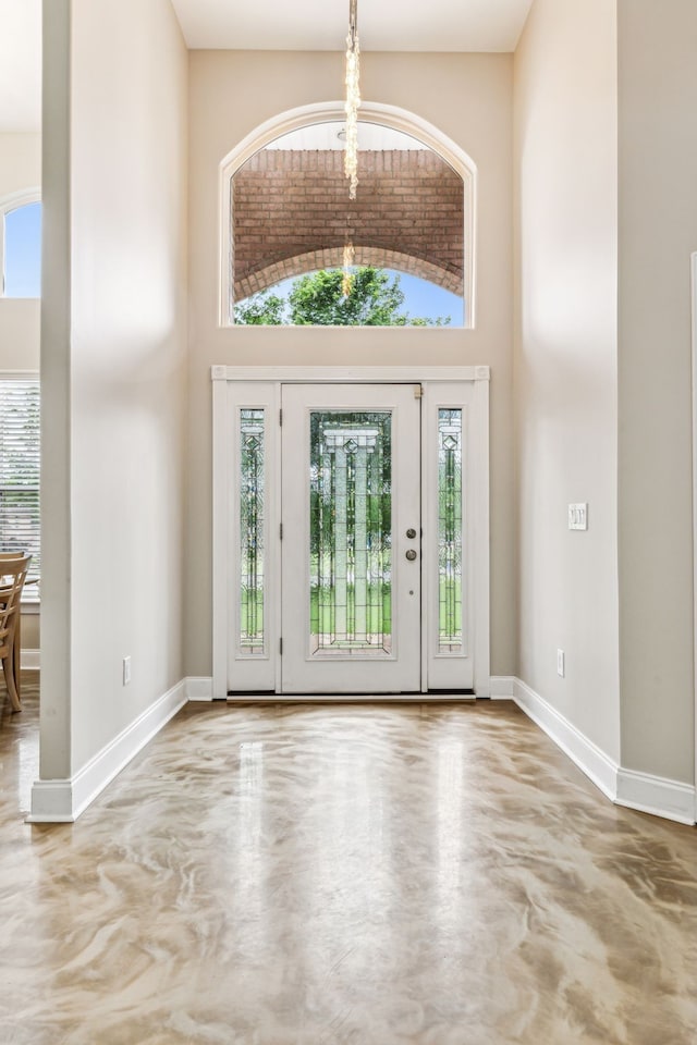 foyer with concrete flooring, a towering ceiling, and a healthy amount of sunlight