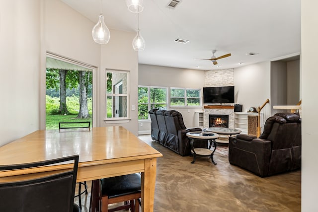 dining space featuring a stone fireplace, ceiling fan, and concrete floors