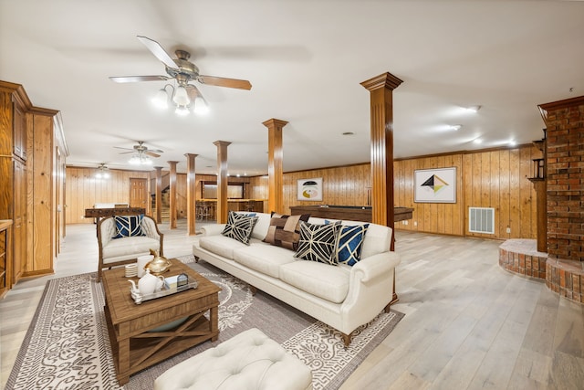 living room with light wood-type flooring, ornate columns, and wooden walls