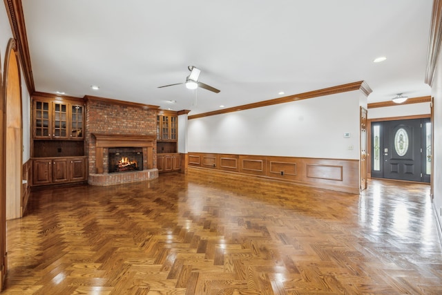 unfurnished living room featuring ceiling fan, ornamental molding, a fireplace, and parquet floors