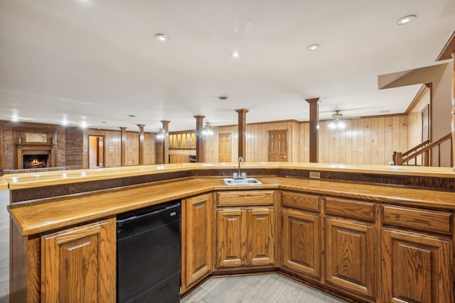 kitchen with dishwasher, sink, wooden walls, light wood-type flooring, and a fireplace