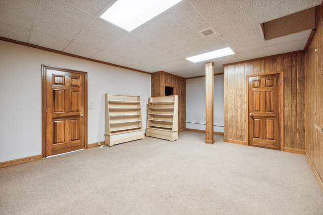 basement featuring crown molding, wooden walls, a drop ceiling, and light colored carpet