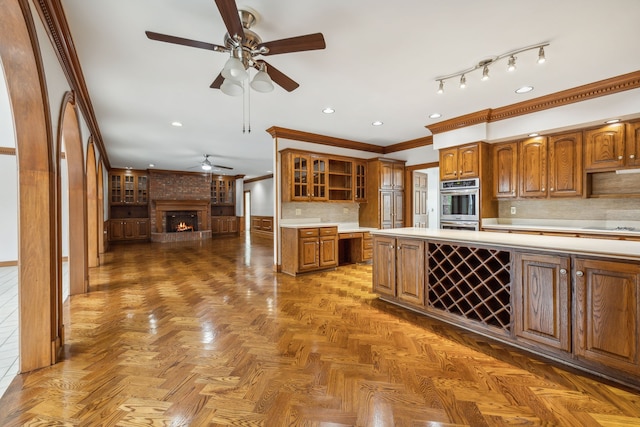 kitchen featuring stainless steel double oven, a brick fireplace, dark parquet floors, backsplash, and ornamental molding