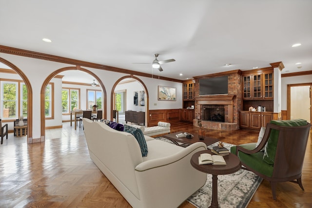 living room with ceiling fan, a fireplace, crown molding, and light parquet floors