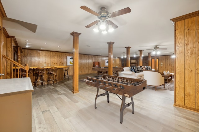 playroom with ornate columns, ceiling fan, wooden walls, indoor bar, and light hardwood / wood-style flooring