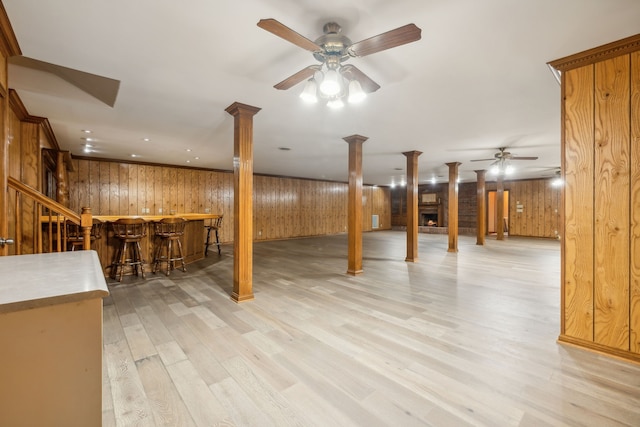 basement featuring bar area, wooden walls, ceiling fan, and light hardwood / wood-style floors