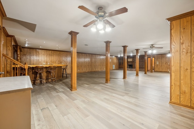 basement with ceiling fan, light hardwood / wood-style flooring, bar, and wood walls