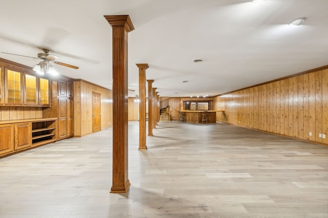 basement with ceiling fan, wood walls, light wood-type flooring, and crown molding