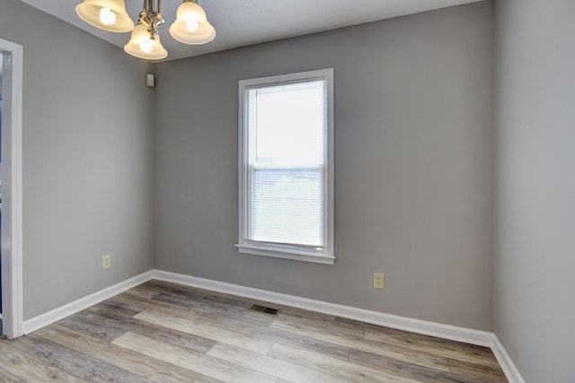 empty room with light hardwood / wood-style floors and an inviting chandelier