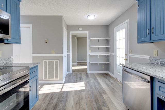 kitchen with blue cabinetry, stainless steel appliances, a textured ceiling, and light hardwood / wood-style floors