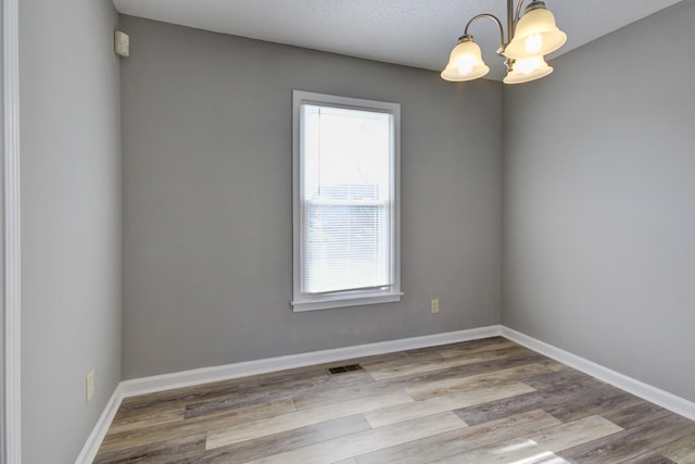 unfurnished room featuring a chandelier, a textured ceiling, and light hardwood / wood-style flooring