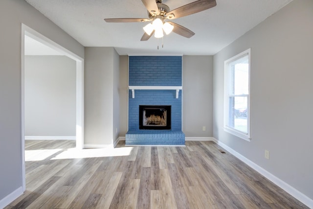 unfurnished living room featuring a brick fireplace, ceiling fan, and light wood-type flooring