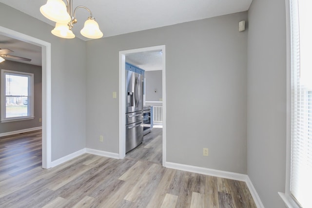 unfurnished dining area featuring ceiling fan with notable chandelier and light wood-type flooring