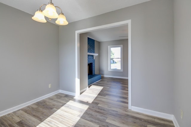 unfurnished dining area featuring a notable chandelier, wood-type flooring, and a brick fireplace