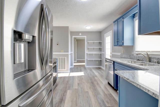 kitchen featuring appliances with stainless steel finishes, a textured ceiling, blue cabinets, sink, and light hardwood / wood-style flooring