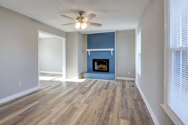 unfurnished living room with ceiling fan, light wood-type flooring, a textured ceiling, and a brick fireplace