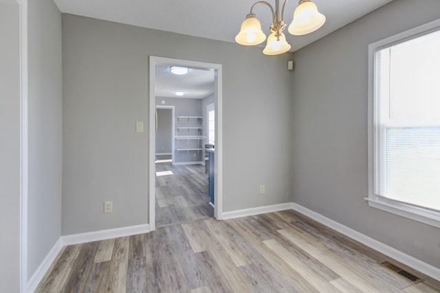 empty room featuring light hardwood / wood-style flooring, a wealth of natural light, and a notable chandelier