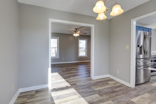 unfurnished dining area featuring ceiling fan with notable chandelier, a textured ceiling, and light hardwood / wood-style floors